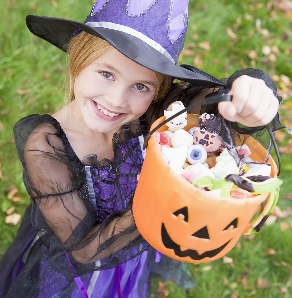 Young Girl Outdoors In Witch Costume On Halloween Holding Candy